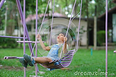 Happy Asian girl having fun playing in the playground during summer. Cute little girl swinging in the playground with a smile and Stock Photo