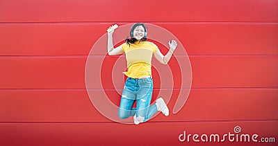 Happy Asian girl jumping while listening music outdoor - Crazy Chinese woman having fun dancing a song against red background Stock Photo