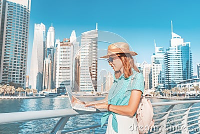 Asian girl works at a laptop in Dubai Marina port against the backdrop of high skyscrapers and the Bay Stock Photo