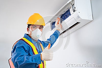 Happy asian male wear a safety mask to prevent dust technician cleaning air conditioner indoors, Air conditioner technician Stock Photo