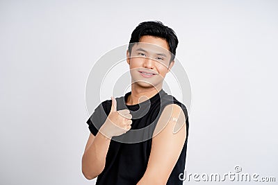 Happy Asian man showing thumbs up and showing shoulder with bandages after getting vaccinated. Vaccine program, Recommended Stock Photo