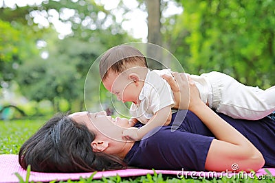 Happy Asian mom embrace her son lying in the green garden. Funny mother and infant baby boy playing in summer park Stock Photo