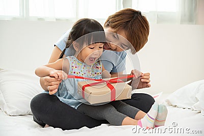 Child daughter unwrapping gift box with her mom. Stock Photo