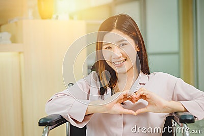 Happy Asian teen girl smile Heart shape hand sitting on wheelchair in hospital Stock Photo