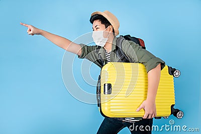 Happy Asian tourists wear protective masks and carry a yellow suitcase on a blue background. Isolated background Stock Photo