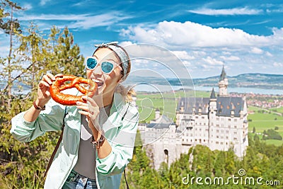 Asian traveller girl eats crispy pretzel in the background of the legendary Neuschwanstein castle. Tourism in Bavaria Stock Photo