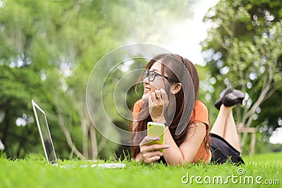 Happy Asian woman resting and looking beside in park with smartphone. People and lifestyles concept. Technology and Beauty theme Stock Photo