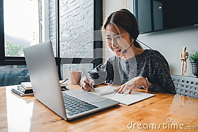 Happy asian woman student watching lesson online and studying from home. Young woman taking notes while looking at Stock Photo