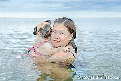 Happy Asian women girl hug play immersed in beach sea water with cute dog puppy pug Stock Photo