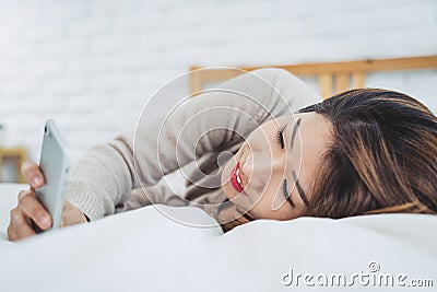 Happy Asian women are using smart phone on the bed in morning. Asian woman in bed checking social apps with smartphone. Stock Photo