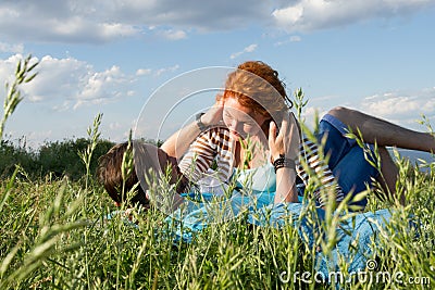 Happy attractive couple on picnic blanket. Couple relaxing together on summer day under clouds in blue sky. Stock Photo