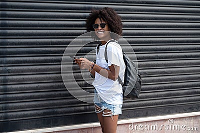 Happy attractive girl in the city street using mobile phone, checking social media and emails. Woman with afro hairstyle in Stock Photo