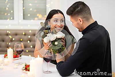 Happy attractive woman holding flowers, looking at her handsome boyfriend Stock Photo