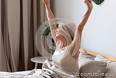 Happy awakened aged woman stretching after night sleeping Stock Photo