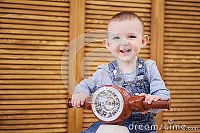 Happy baby boy rides a plastic children motorcycle in the playroom. A Stock Photo