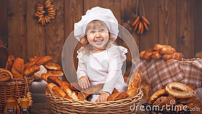 Happy baby chef in wicker basket laughing playing chef in bakery, lots of bread baking. Stock Photo