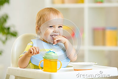 Happy baby kid boy eating itself with spoon Stock Photo