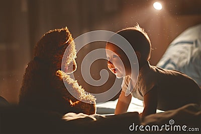 Happy baby laughing with teddy bear in bed Stock Photo