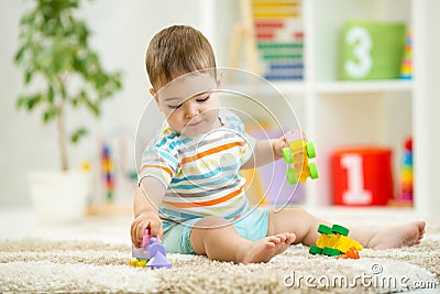 Happy baby playing with colorful plastic bricks on the floor. Toddler having fun and building a train out of constructor Stock Photo