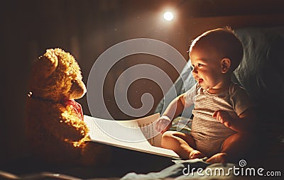 Happy baby reading a book with teddy bear in bed Stock Photo