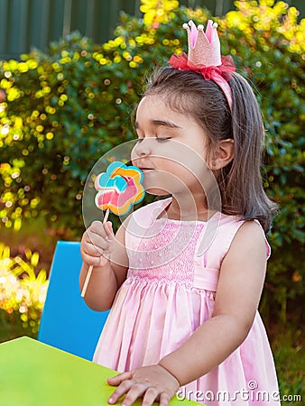 Happy baby toddler girl smelling and savoring a large colorful lollipop smell, scent or aroma Stock Photo