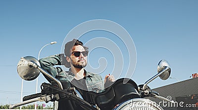 Happy bearded biker staying with unknown big chopper bike on road with helmet on hand. Stock Photo