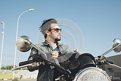 Happy bearded biker staying with unknown big chopper bike on road with helmet on hand. Stock Photo