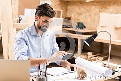 Happy bearded timber craftsman using modern gadget in his work Stock Photo