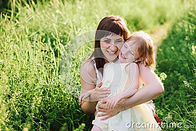 Happy beatiful Mom kisses and hugs daughter on nature in sunset light Stock Photo