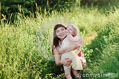 Happy beatiful Mom kisses and hugs daughter on nature in sunset light Stock Photo