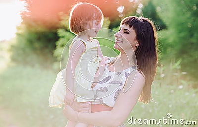 Happy beatiful Mom kisses and hugs daughter on nature in sunset light Stock Photo