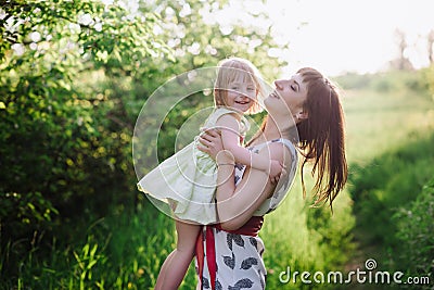 Happy beatiful Mom kisses and hugs daughter on nature in sunset light Stock Photo