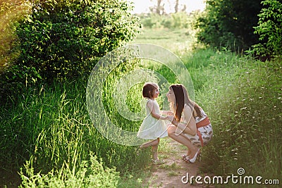 Happy beatiful Mom kisses and hugs daughter on nature in sunset light Stock Photo