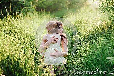 Happy beatiful Mom kisses and hugs daughter on nature in sunset light Stock Photo