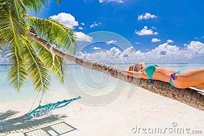 Woman in hot sunny weather laying down on a palm tree and enjoying tropical beach vacation, carefree holiday Stock Photo