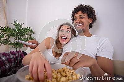 Happy beautiful couple eating popcorn while watching TV in bed Stock Photo