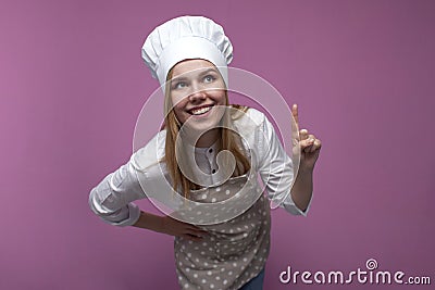 Happy beautiful girl cook in kitchen clothes thinks over an idea on a pink background, a woman housewife dreams and looks at a Stock Photo