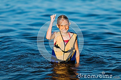 Happy beautiful little girl in a life jacket, swimming in the sea and showing a winning gesture. Summer holiday, vacation Stock Photo