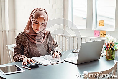 Happy beautiful muslim business woman brown hijab working about financial with business report and calculator in home office Stock Photo