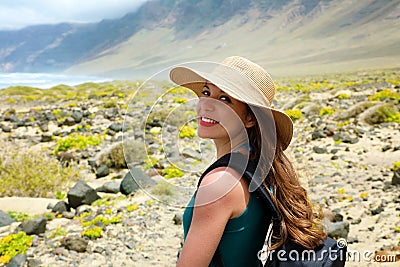 Happy beautiful traveler girl with straw hat looking to the camera. Young female backpacker exploring Lanzarote, Canary Islands. Stock Photo