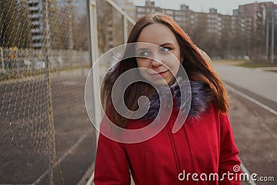 Happy beautiful young girl in a red jacket posing outside on a cloudy day Stock Photo