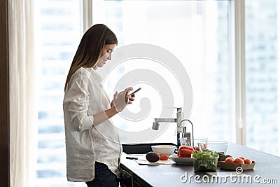 Happy beautiful young smartphone user girl reading recipe on internet Stock Photo