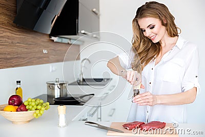 Happy beautiful young woman cooking meat on the kitchen Stock Photo