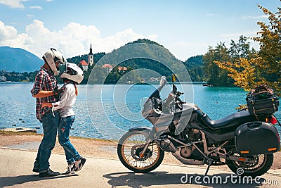 Happy biker couple in love travel together. Stands by a motorcycle with bags. Tourism and vacation. Sunny summer day. Bled lake, Stock Photo
