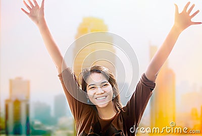Happy biracial teen girl arms raised, skyscapers in background Stock Photo