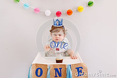 Happy birthday party. Cute Caucasian baby boy in blue crown celebrating first birthday at home. Child toddler in a high chair Stock Photo