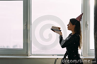 Happy birthday, woman holding cake looking at candle, window background, profile view Stock Photo