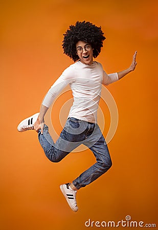 Happy black guy jumping on orange studio background Editorial Stock Photo