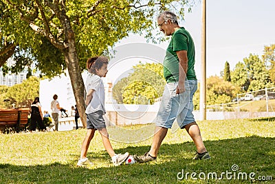 Happy black little boy and man with beard play ball football in park, enjoy sport competition Stock Photo