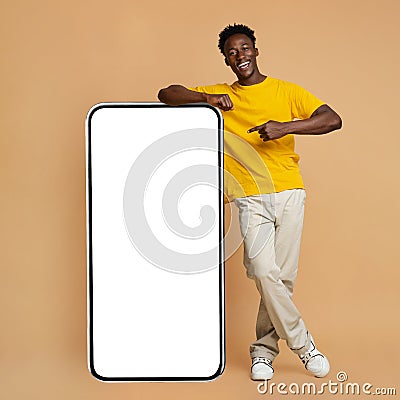 Happy Black Man Leaning And Pointing At Big Smartphone With White Screen Stock Photo